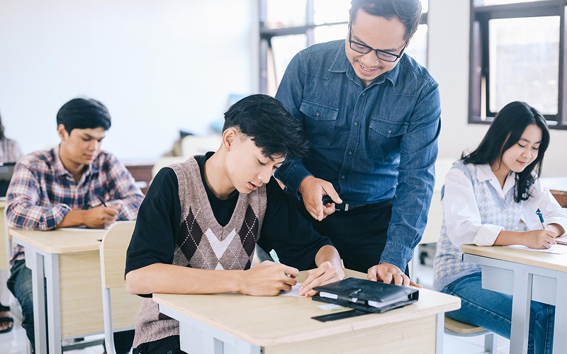 Teacher assisting high school student earning his diploma in class.